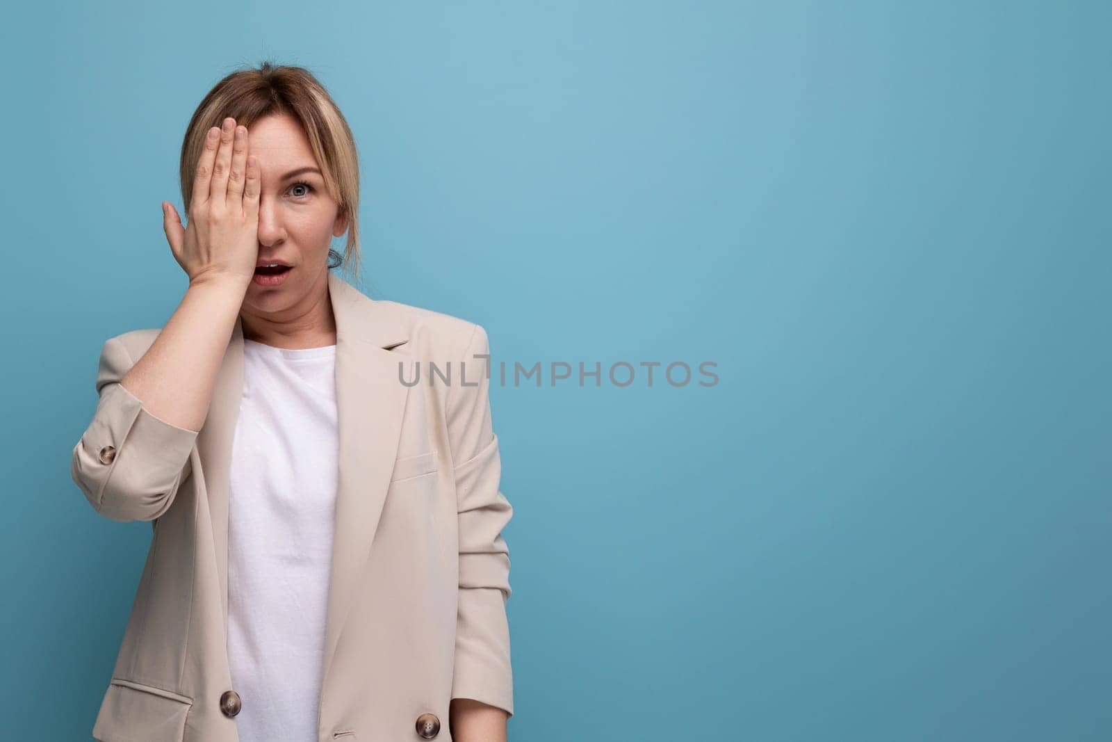 close-up of a blonde woman in an office jacket standing thoughtfully on a blue background with copy space.