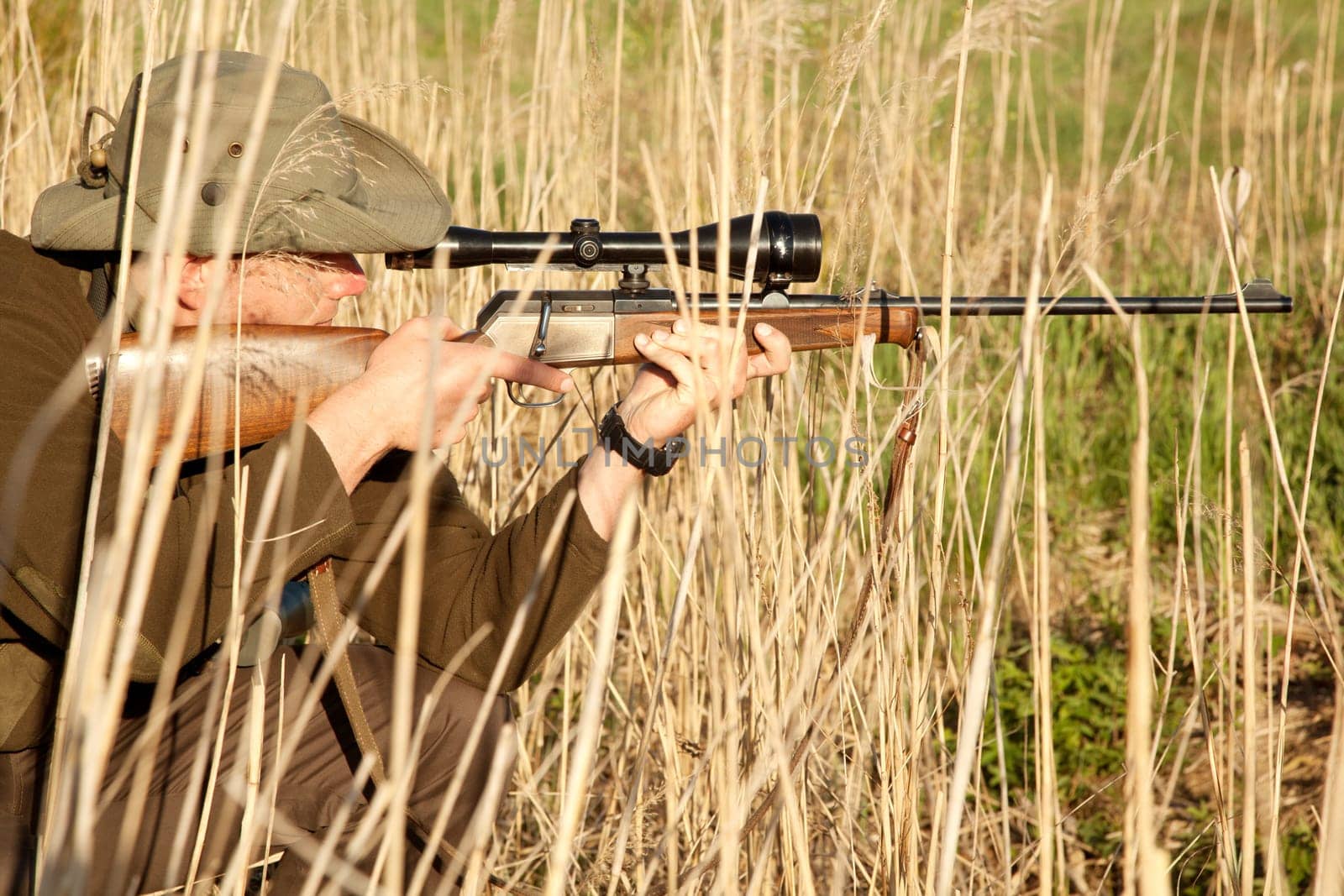Nature, wildlife and male hunter with a shotgun while in camouflage shooting in outdoor field. Grass, safari and man hunting animals with rifle weapon hiding in plants to shoot target in countryside