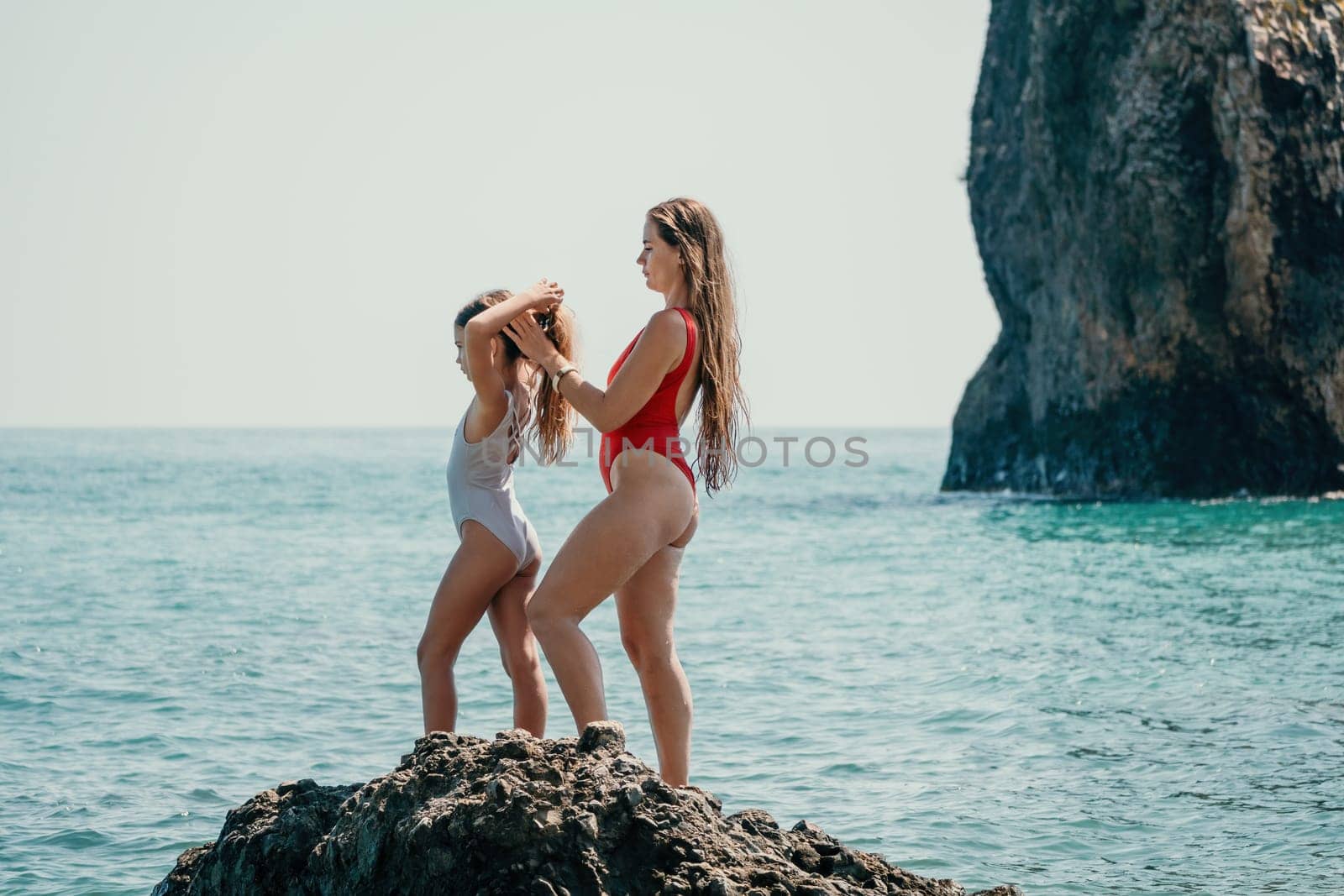 Woman and her daughter together on rock in the sea.
