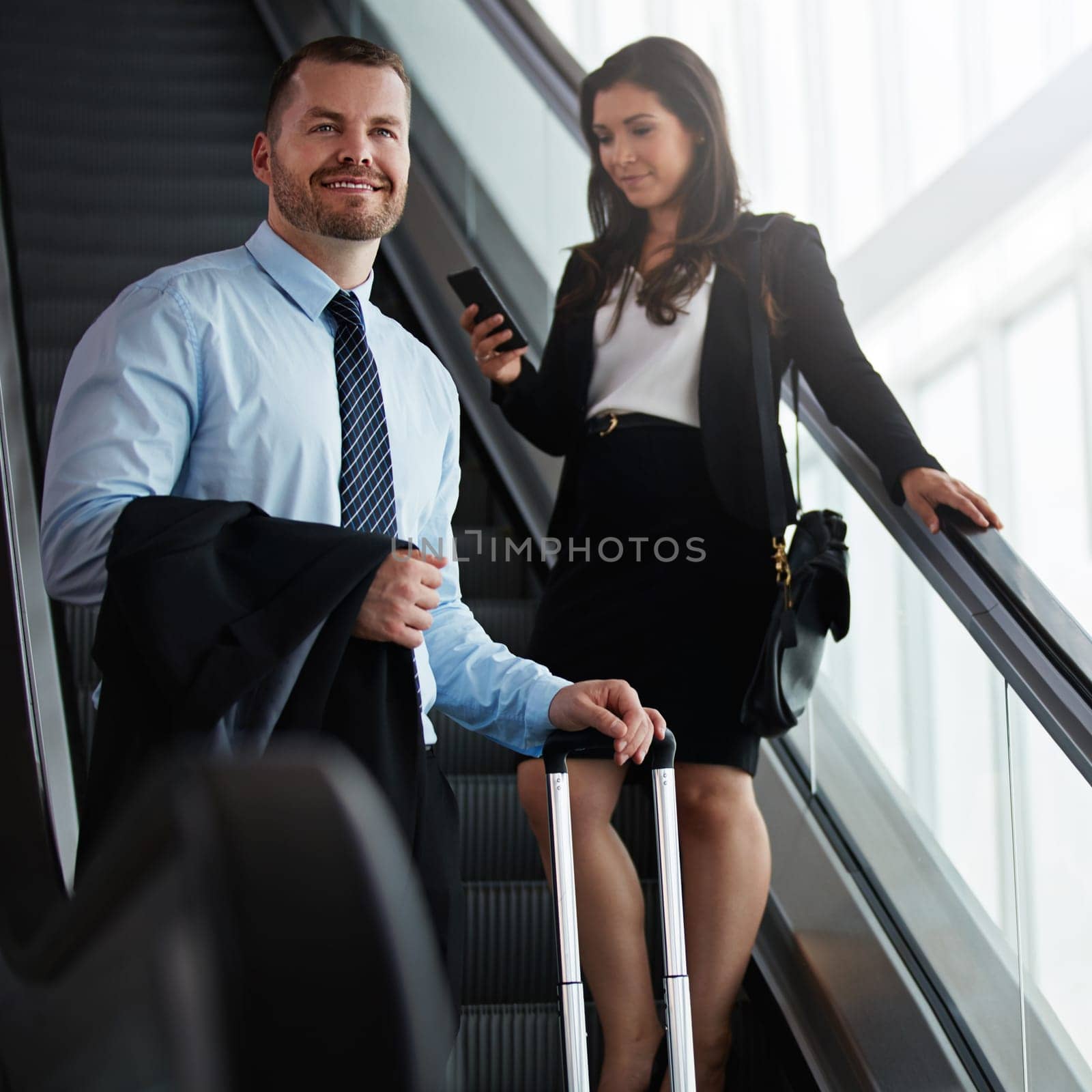 Well seasoned business travelers. a businessman traveling down an escalator in an airport with a businesswoman behind him. by YuriArcurs