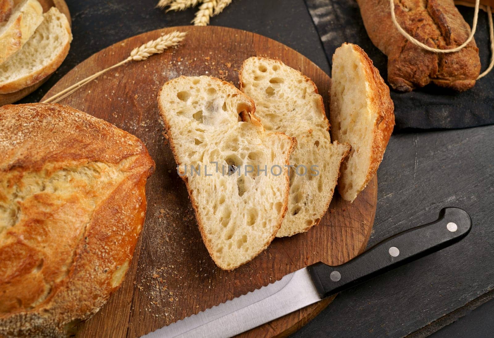 Round loaf of freshly baked sourdough bread with knife on cutting board. Concept of homemade bread, natural farm products, domestic production. Healthy and tasty organic food. Fresh bread slice and cutting knife on rustic table