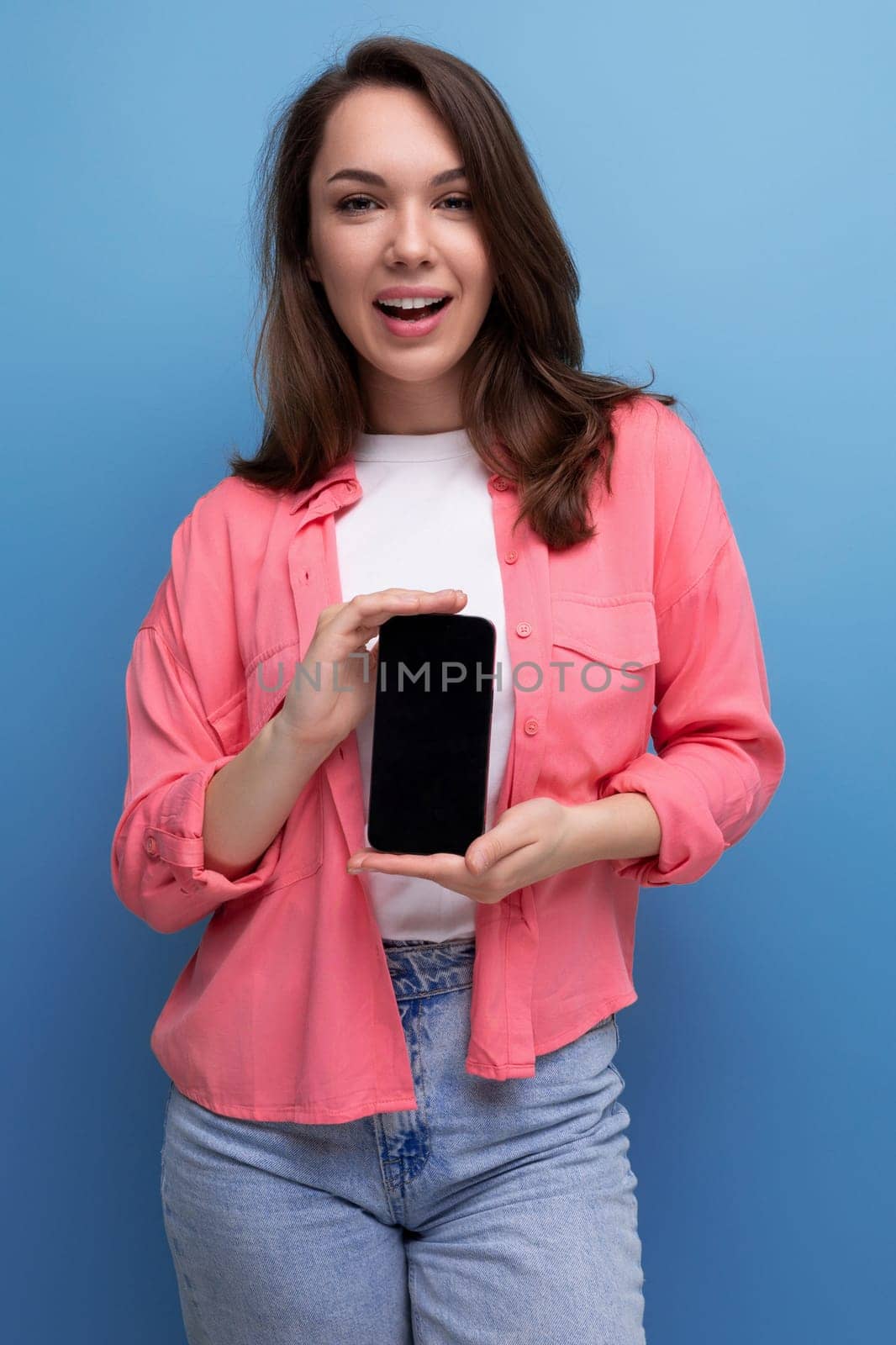 a smiling brunette lady with dark hair below her shoulders in a shirt and jeans demonstrates a smartphone screen forward by TRMK