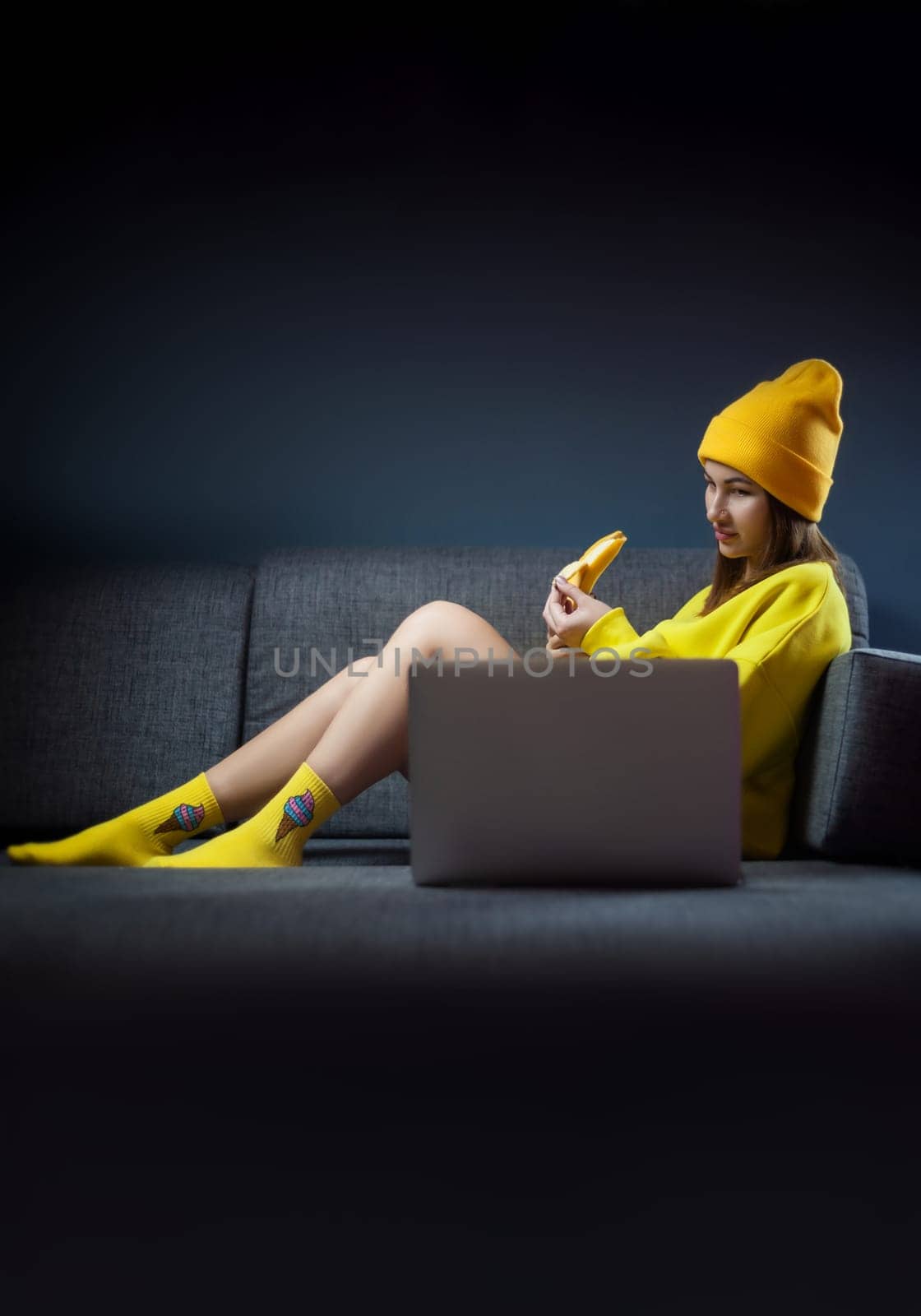 sexy girl in yellow clothes and a hat with a banana and a laptop on dark background copy paste