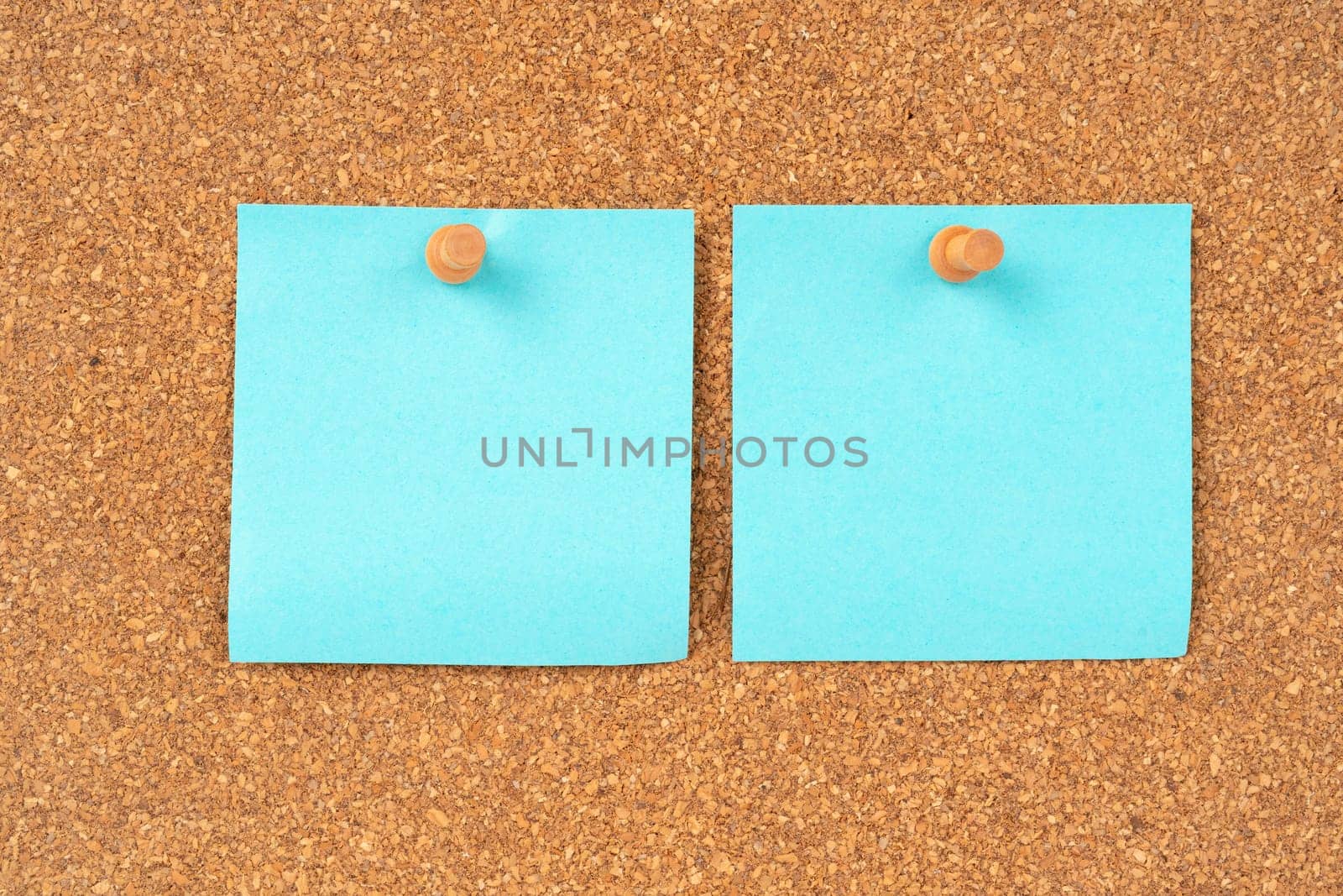 Blank blue color sticky note paper and wooden thumbtack on wooden background.