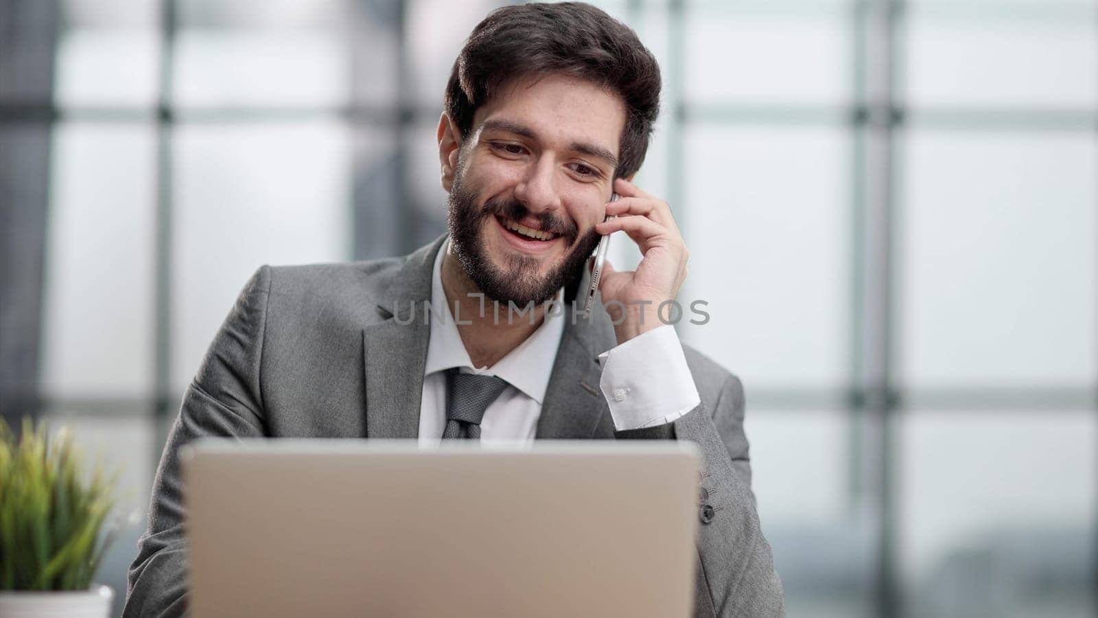 Smiling man while making phone call and using laptop in the office