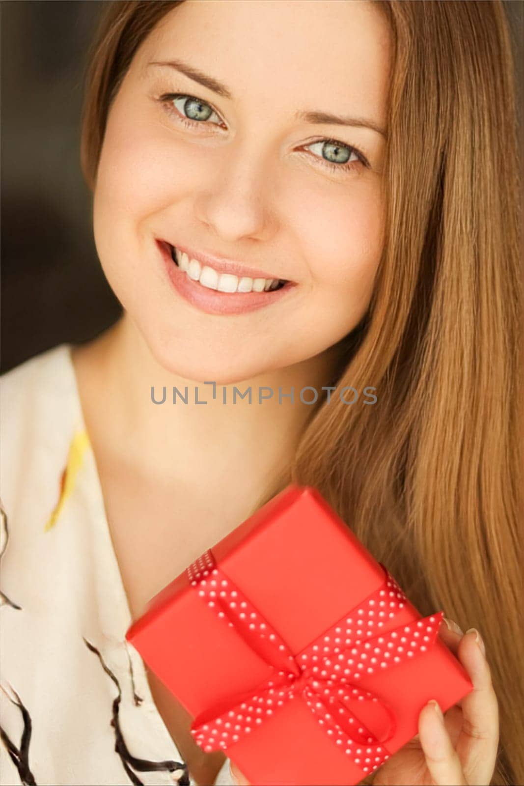 Happy smiling woman holding a red gift box, face portrait with natural make-up and holiday lifestyle mood at home.