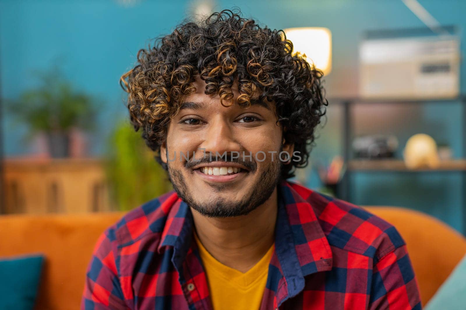 Portrait of happy calm indian man at home couch smiling friendly, glad expression looking away dreaming resting, relaxation feel satisfied concept good news, celebrate win. Hindu guy in living room
