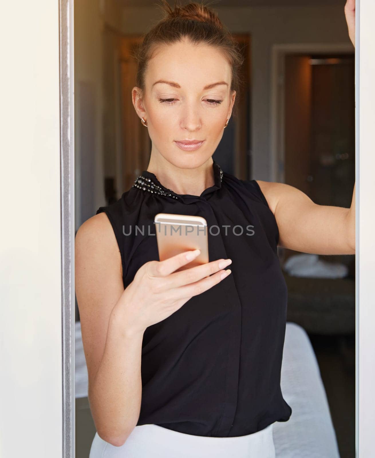 Sending a quick text. a young woman using her cellphone in her hotel room. by YuriArcurs