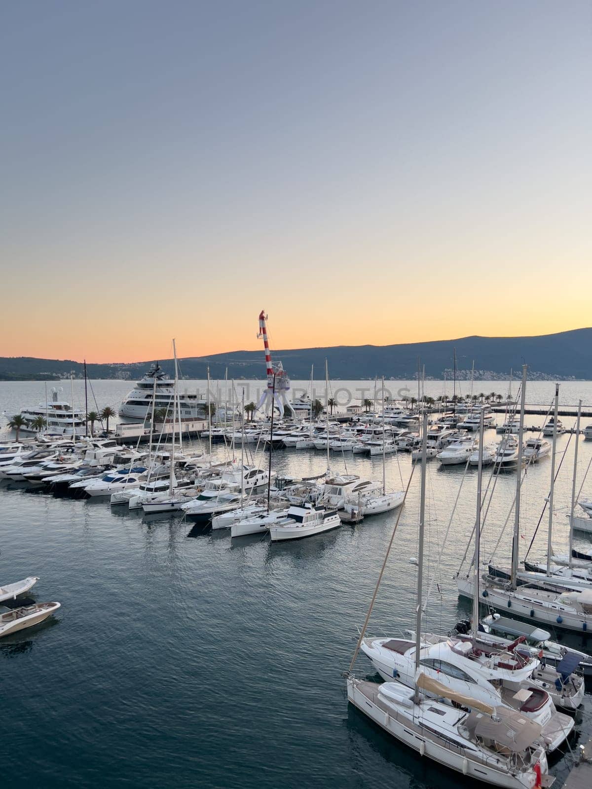 Crane stands on a pier among moored yachts against the backdrop of mountains at sunset. High quality photo