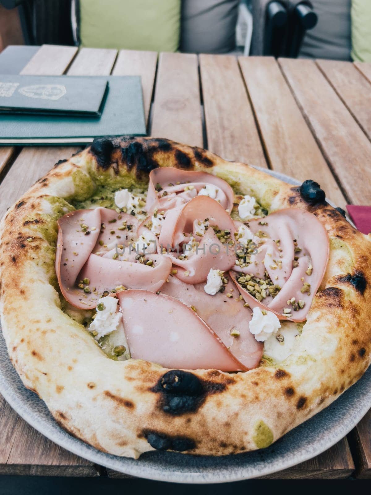 Pizza with mortadella on a thick crust lies on a plate on a wooden table. High quality photo