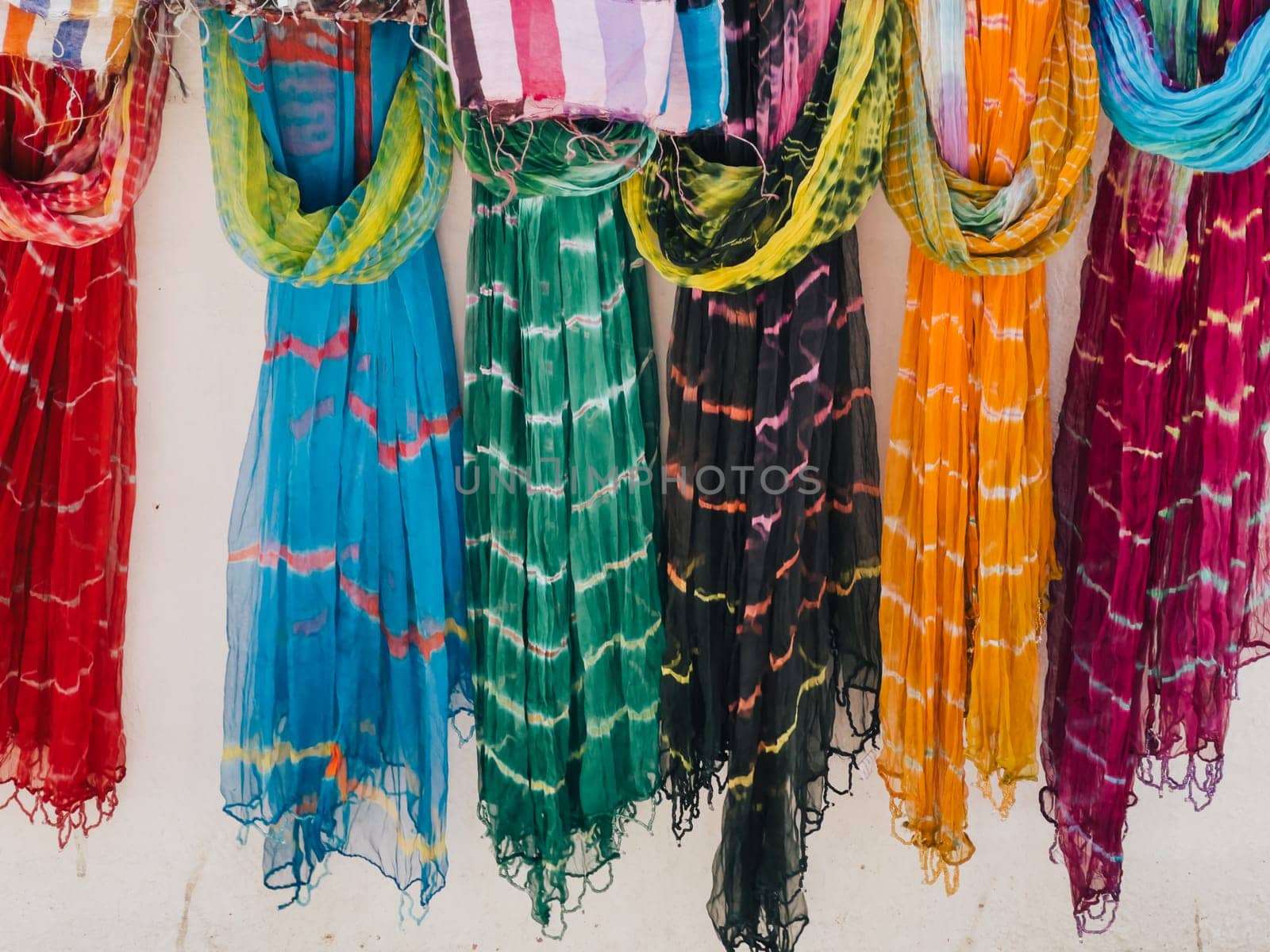 Multi-colored chiffon scarves hang on hangers along a white wall. High quality photo