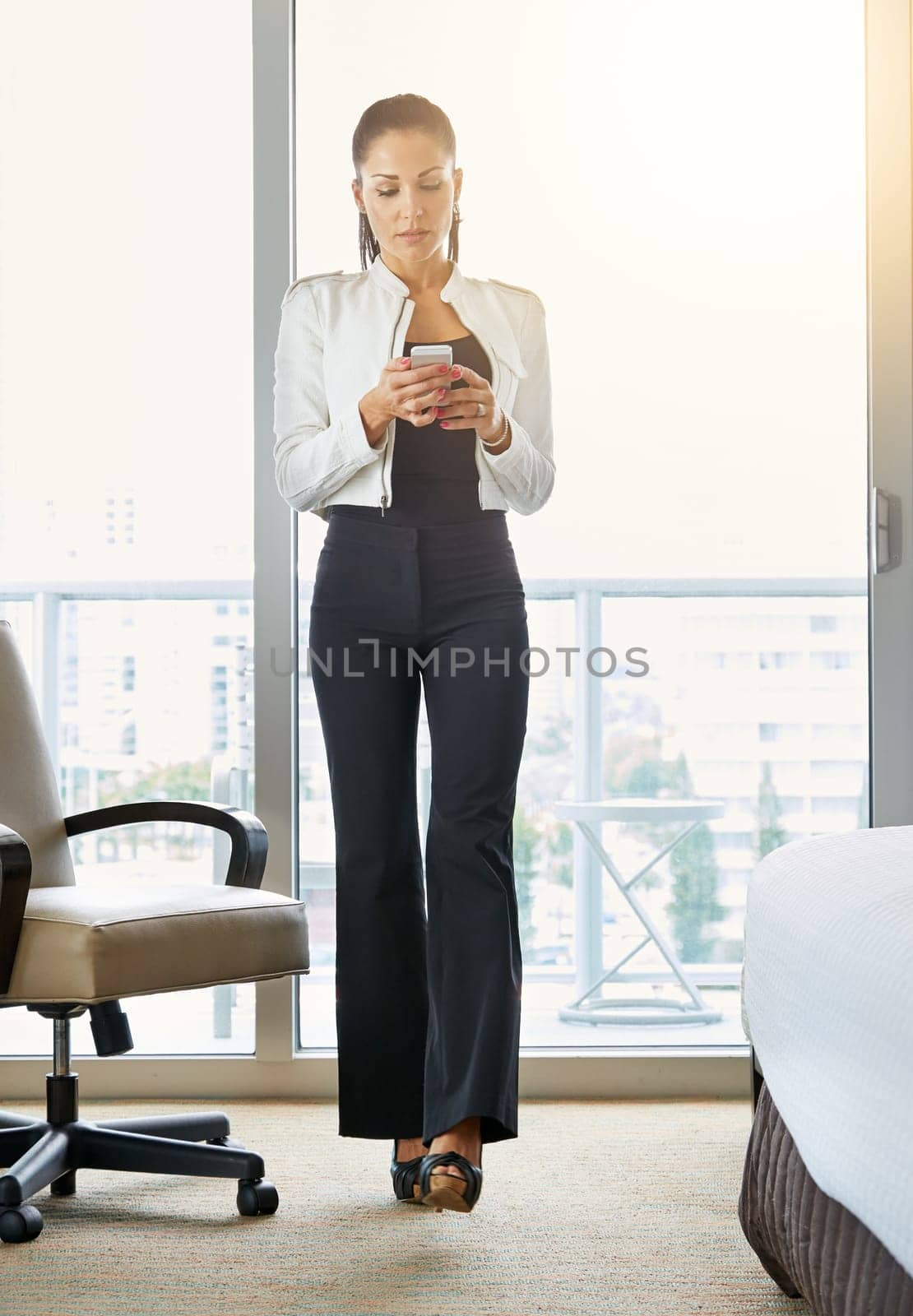 Organizing her day from the hotel suite. a young businesswoman using her cellphone in the hotel room. by YuriArcurs