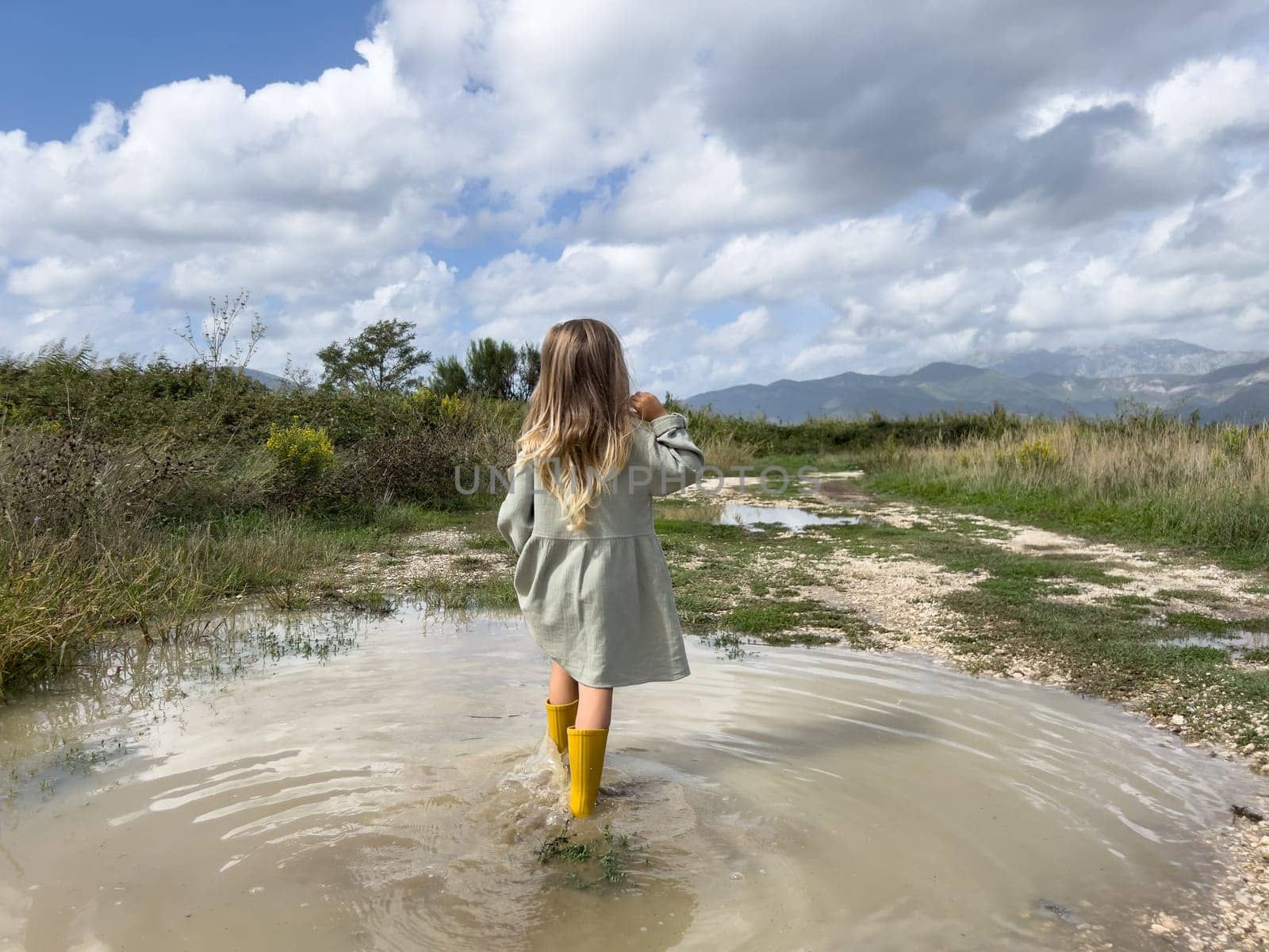 Little girl walks through a puddle to a country road and looks at the mountains. High quality photo