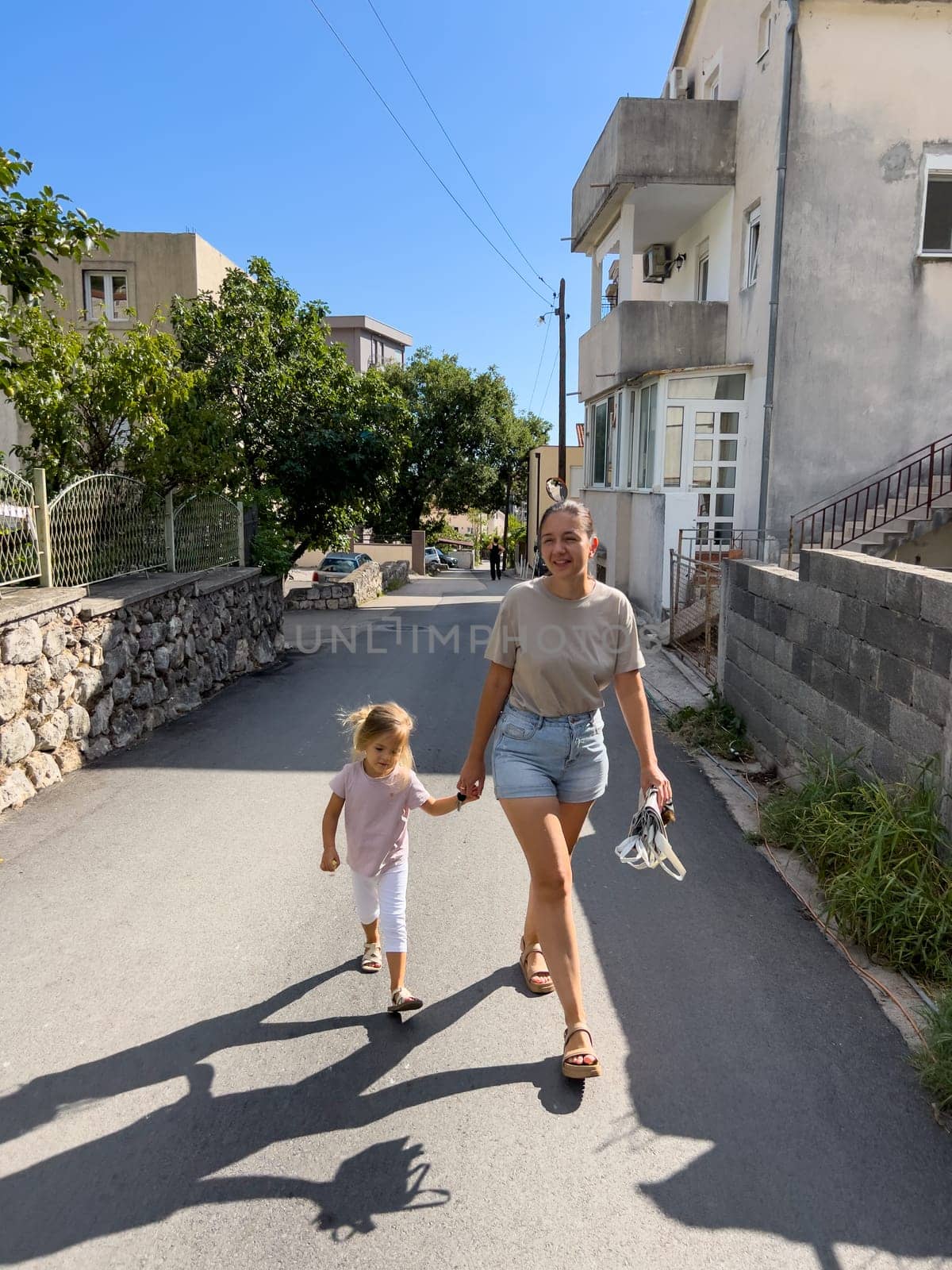Mom and a little girl walk holding hands along the street of a small town. High quality photo