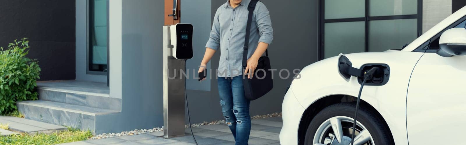 Progressive asian man and electric car with home charging station. Concept of the use of electric vehicles in a progressive lifestyle contributes to a clean and healthy environment.