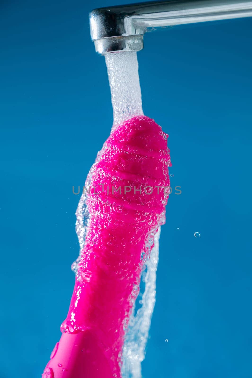 Pink vibrator under running water on a blue background. Sex toy hygiene concept