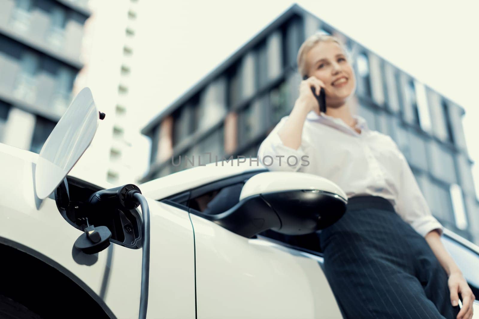 Focus electric car at charging station with blur background of progressive woman by biancoblue