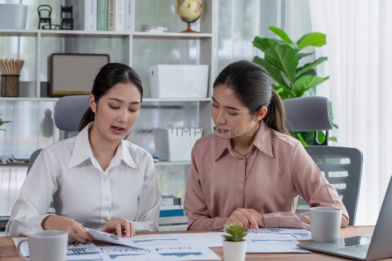 Two young office lady colleagues collaborating in modern office workspace, engaging in discussion and working together on laptop, showcasing their professionalism as modern office worker. Enthusiastic