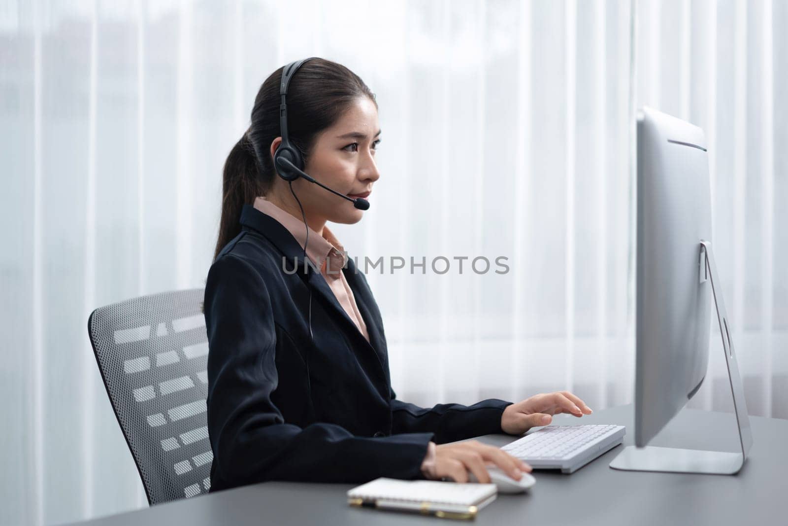 Asian call center with headset and microphone working on her laptop. Female operator provide exceptional customer service. Supportive call center agent helping customer on inquiry. Enthusiastic