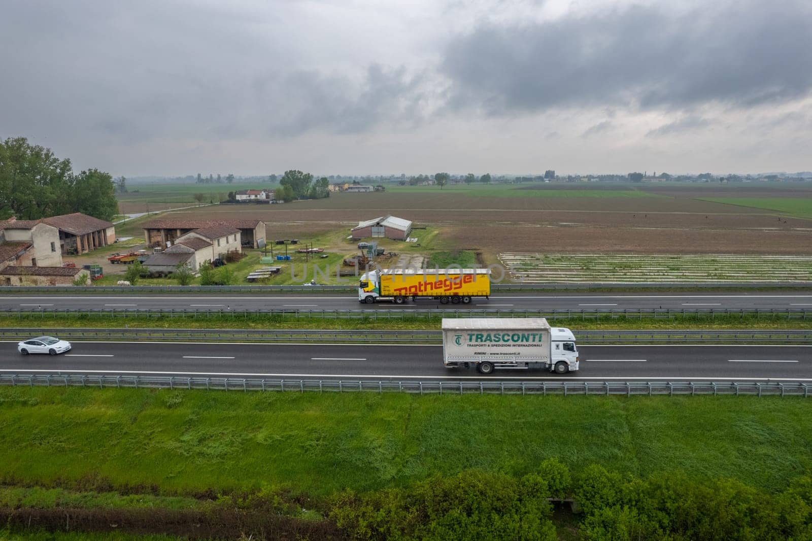 Piacenza, Italy - April 2023 Cargo trucks and cars in the motorway a1 autostrada del sole aerial point of view in between padain plain rural fields