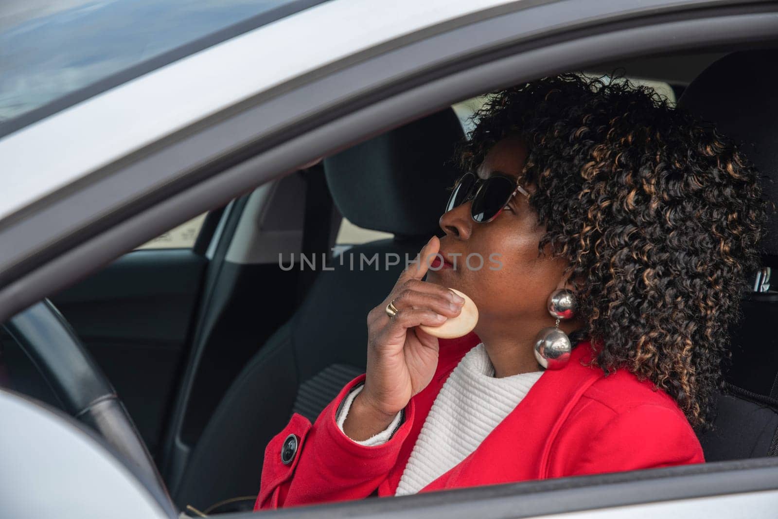 Pretty african american woman in a car doing makeup while standing in a traffic jam, concept a modern married business woman with children saves time, High quality photo