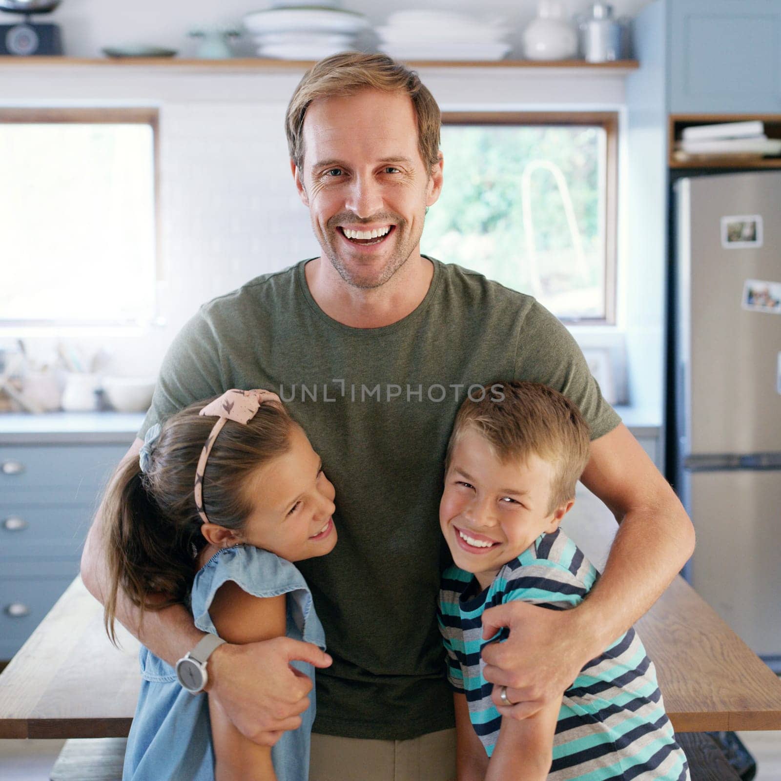Hes a proud father. an affectionate young father embracing his two kids in their kitchen at home. by YuriArcurs