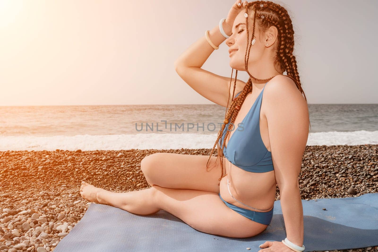 Woman yoga sea. Well looking middle aged woman with braids dreadlocks in white leggings and tops doing stretching pilates on yoga mat near sea. Female fitness yoga routine concept. Healthy lifestyle