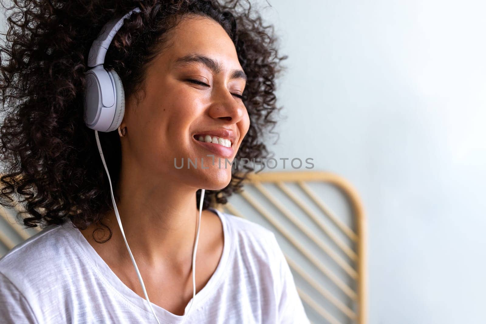 Happy young African American latina woman listening to music using white headphones at home bedroom. Copy space. Lifestyle concept.