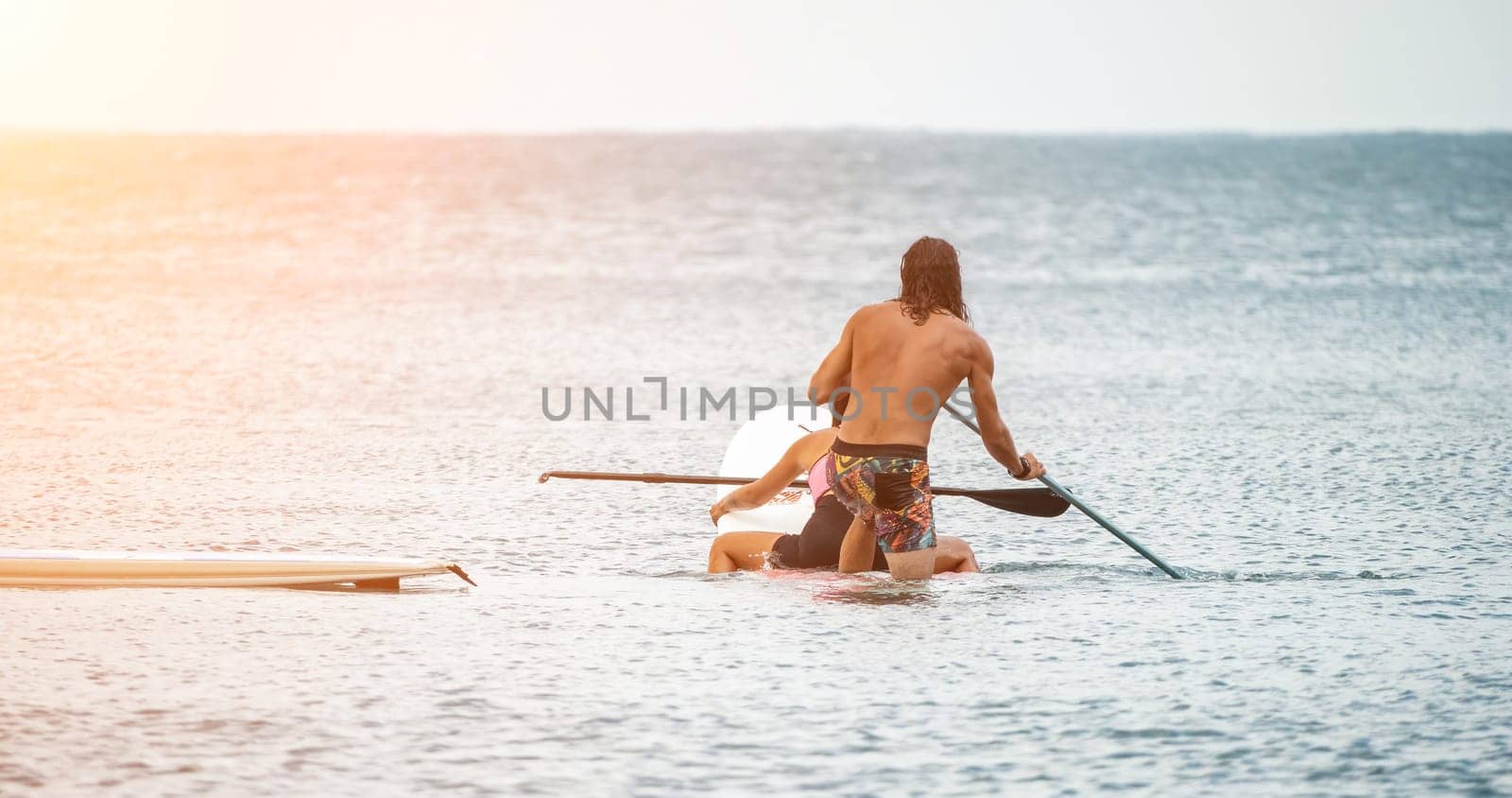 Sea woman and man on sup. Silhouette of happy young woman and man, surfing on SUP board, confident paddling through water surface. Idyllic sunset. Active lifestyle at sea or river. by panophotograph