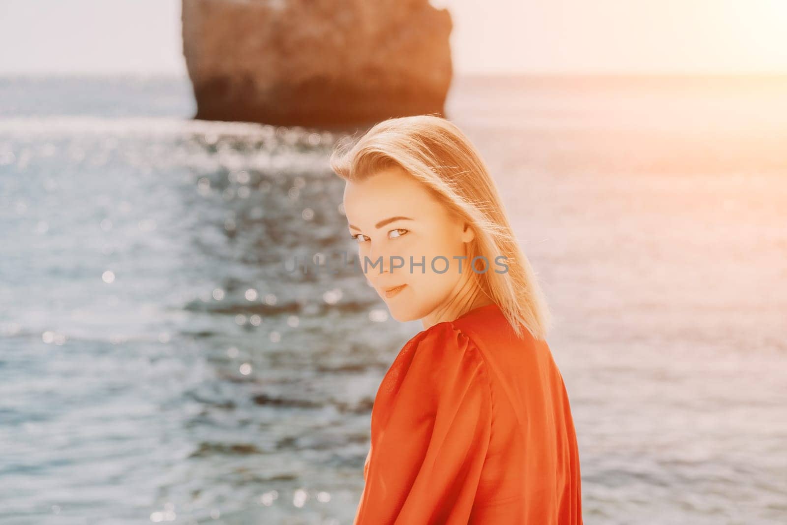 Woman summer travel sea. Happy tourist in long red dress enjoy taking picture outdoors for memories. Woman traveler posing on beach at sea surrounded by volcanic mountains, sharing travel adventure by panophotograph