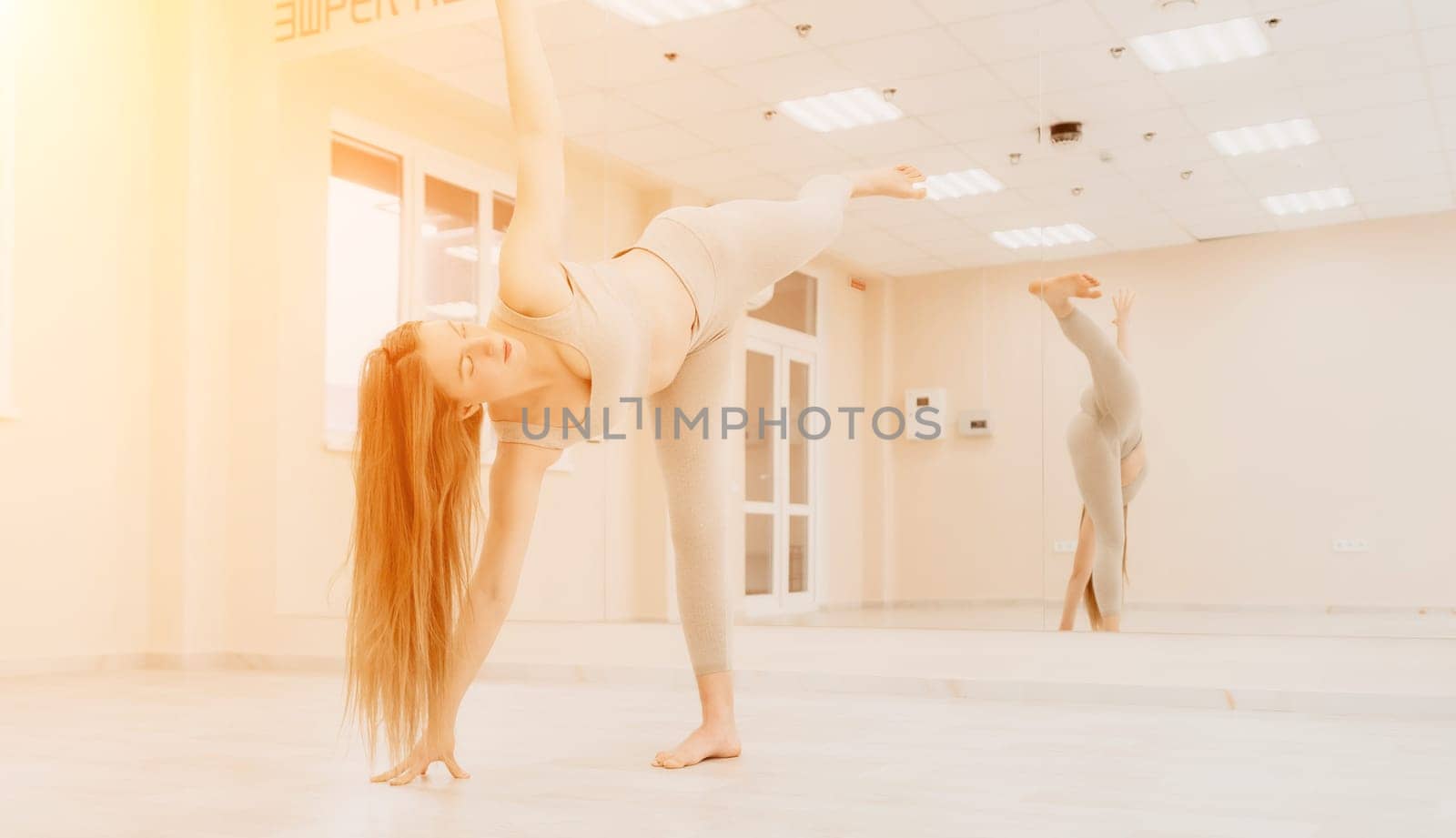 Young sporty woman, fitness instructor in sportswear doing stretching and pilates on yoga mat in the studio with mirror. Female fitness yoga routine concept. Healthy lifestyle and harmony. by panophotograph