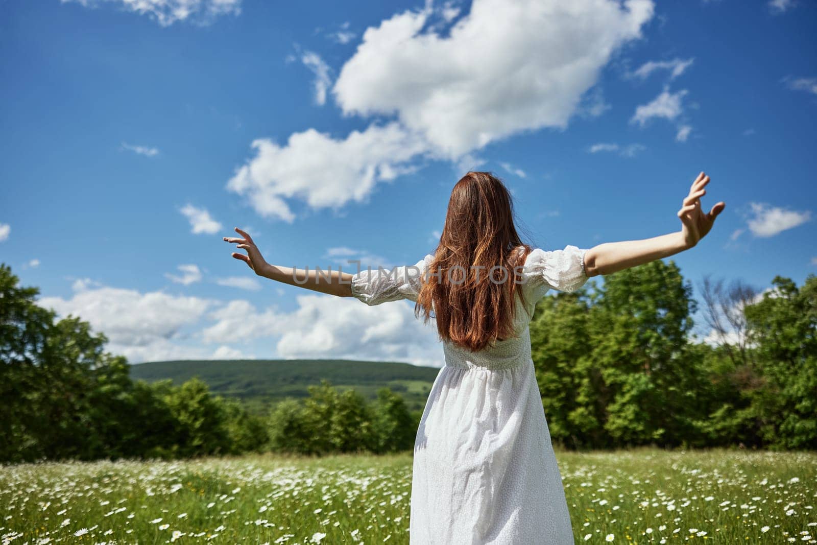 a woman stands with her back to the camera in a light dress in a chamomile field with her hands raised above her head by Vichizh