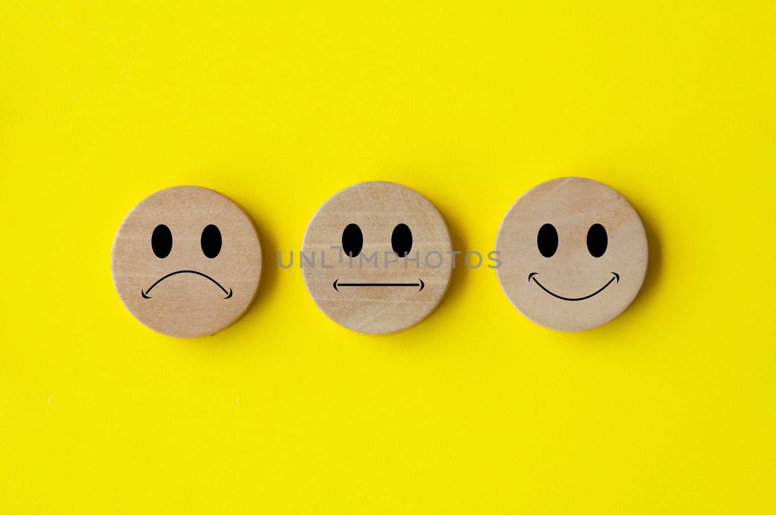 Happy, sad and neutral emoticon faces on wooden circle with yellow background cover. Customer feedback, satisfaction and evaluation and concept.