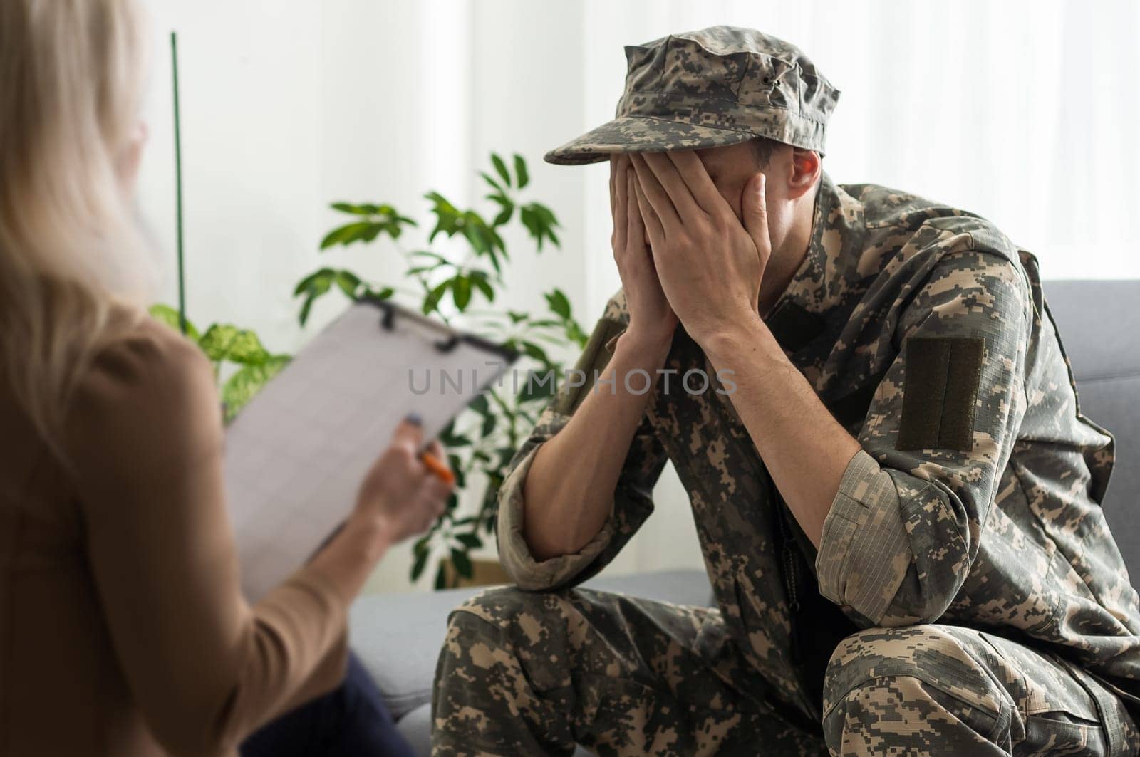 sad soldier with ptsd talking at psychiatrist and gesturing while sitting on couch during therapy session.