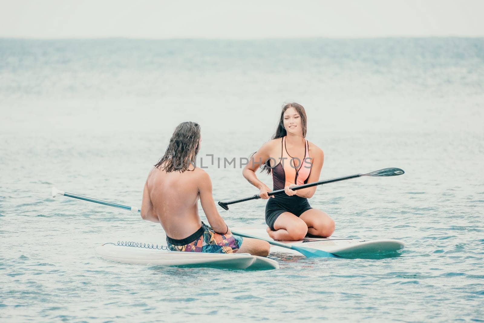 Sea woman and man on sup. Silhouette of happy young woman and man, surfing on SUP board, confident paddling through water surface. Idyllic sunset. Active lifestyle at sea or river