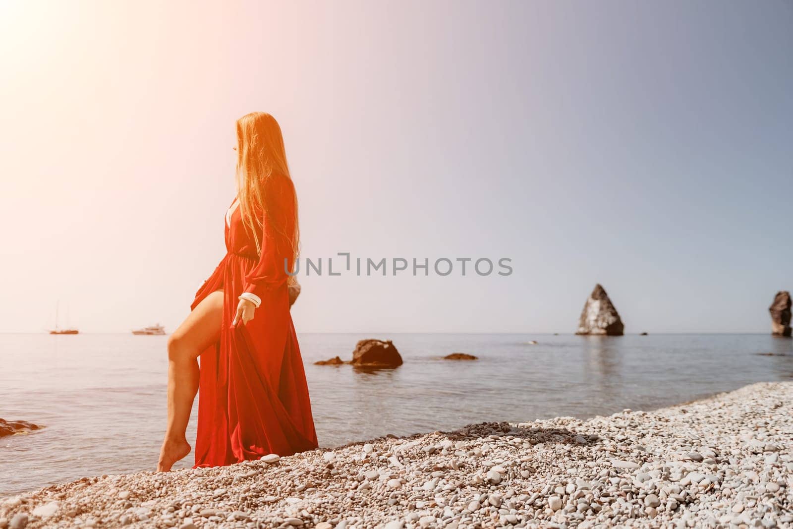 Woman travel sea. Happy tourist in red dress enjoy taking picture outdoors for memories. Woman traveler posing on the rock at sea bay surrounded by volcanic mountains, sharing travel adventure journey by panophotograph