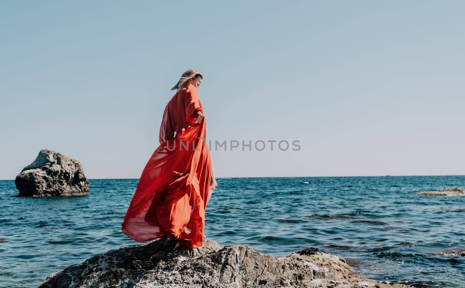 Woman travel sea. Happy tourist in long red dress enjoy taking picture outdoors for memories. Woman traveler posing on beach at sea surrounded by volcanic mountains, sharing travel adventure journey by panophotograph