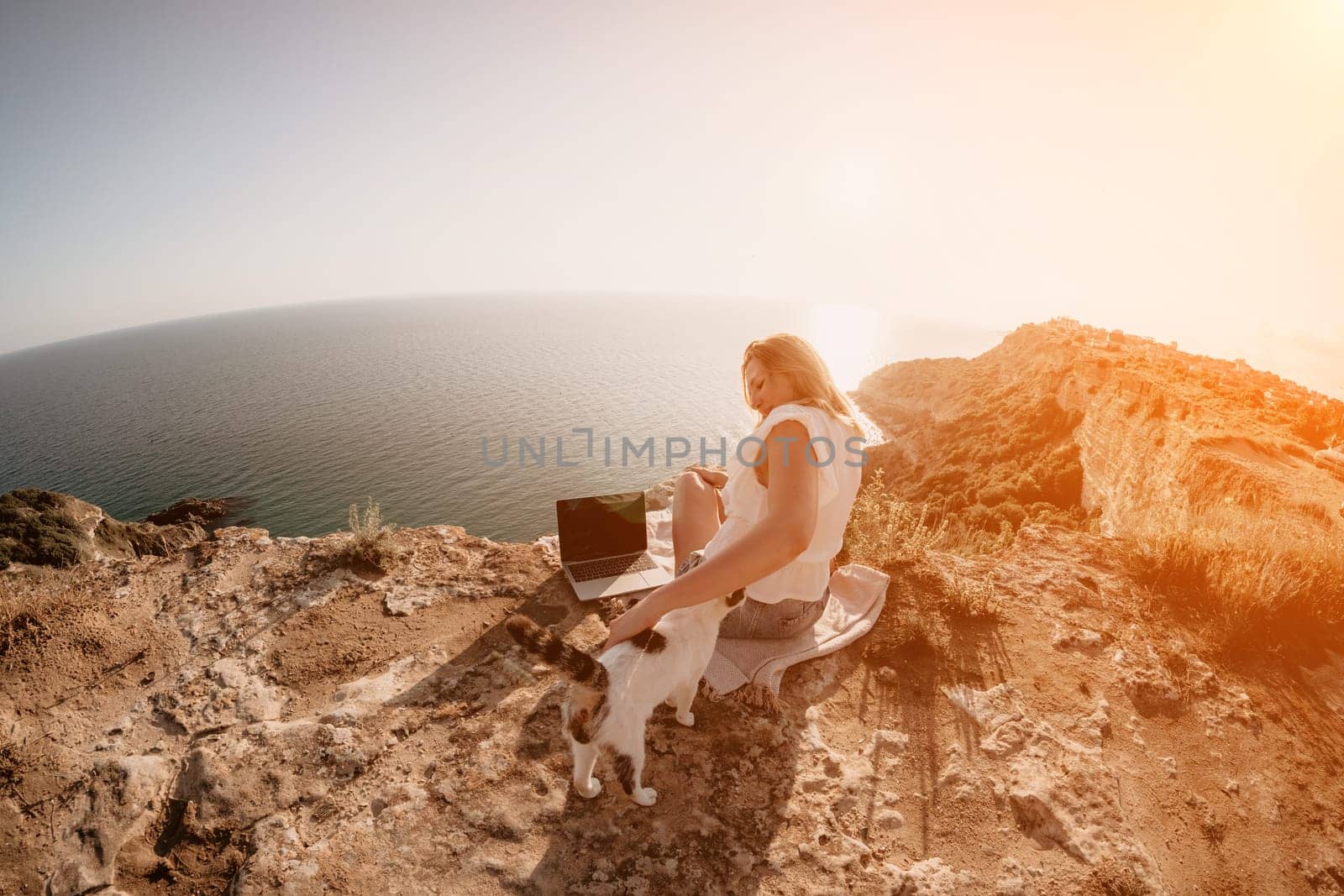 Woman sea laptop. Business woman petting cat and working on laptop by the sea. Close up on hands of pretty lady typing on computer outdoors summer day. Freelance, digital nomad and holidays concept. by panophotograph