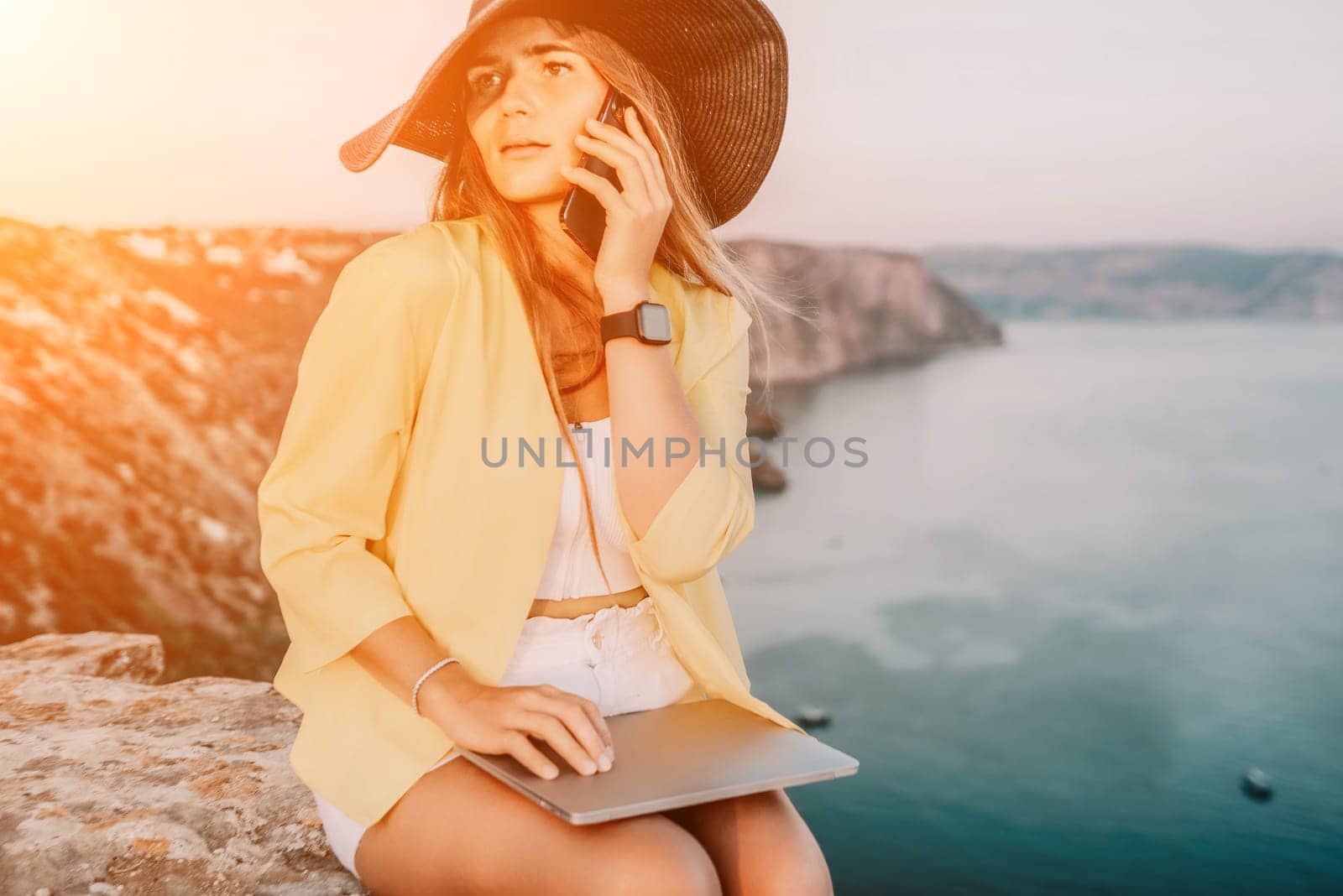 Digital nomad, Business woman working on laptop by the sea. Pretty lady typing on computer by the sea at sunset, makes a business transaction online from a distance. Freelance, remote work on vacation by panophotograph