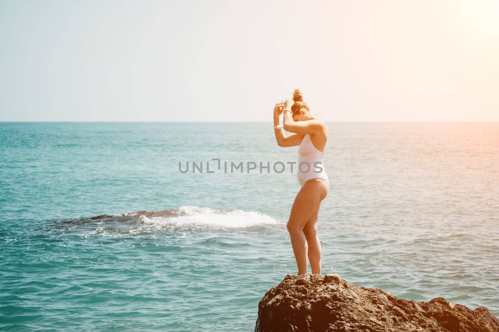 Woman sea yoga. Back view of free calm happy satisfied woman with long hair standing on top rock with yoga position against of sky by the sea. Healthy lifestyle outdoors in nature, fitness concept. by panophotograph