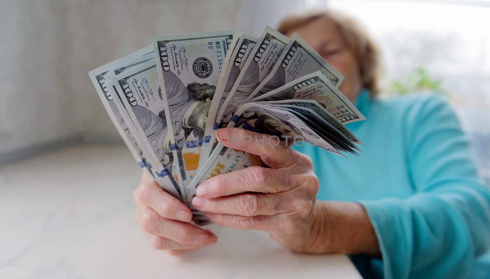 Close-up of an elderly woman's hands holding money in 100 dollar bills, compensation.