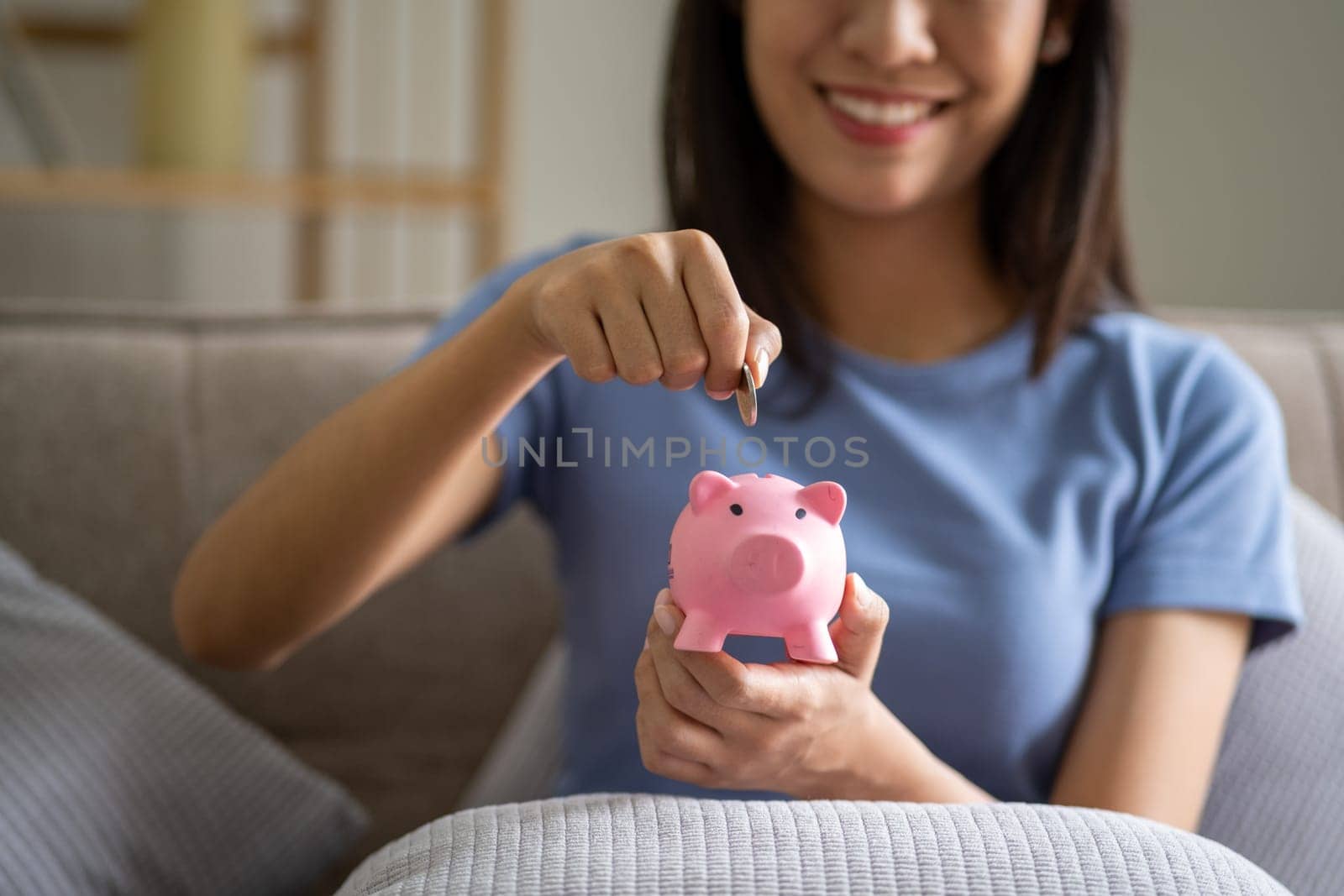 Young smart Asian teenager putting coin in a piggy bank, happy young woman who puts coin in piggy bank for saving, investment economical. High quality photo