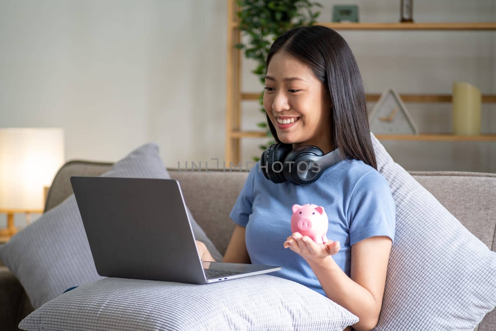 Young smart Asian teenager putting coin in a piggy bank, happy young woman who puts coin in piggy bank for saving, investment economical. High quality photo