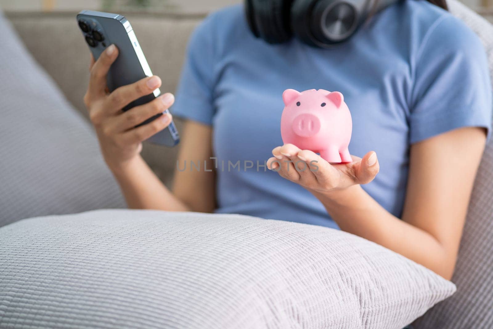 Young smart Asian teenager putting coin in a piggy bank, happy young woman who puts coin in piggy bank for saving by wuttichaicci