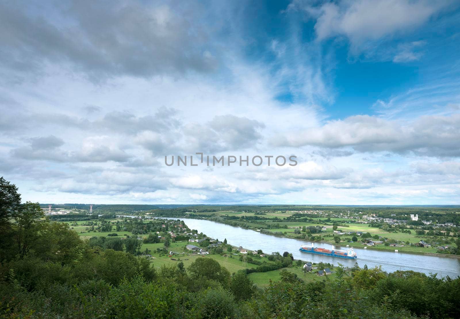 countryside landscape with river seine in france between rouen and le havre with countainer barge heading west