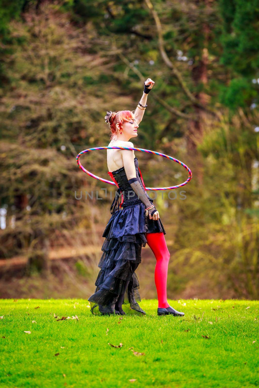 Young beautiful woman in circus costume play with hula hoop in the park.