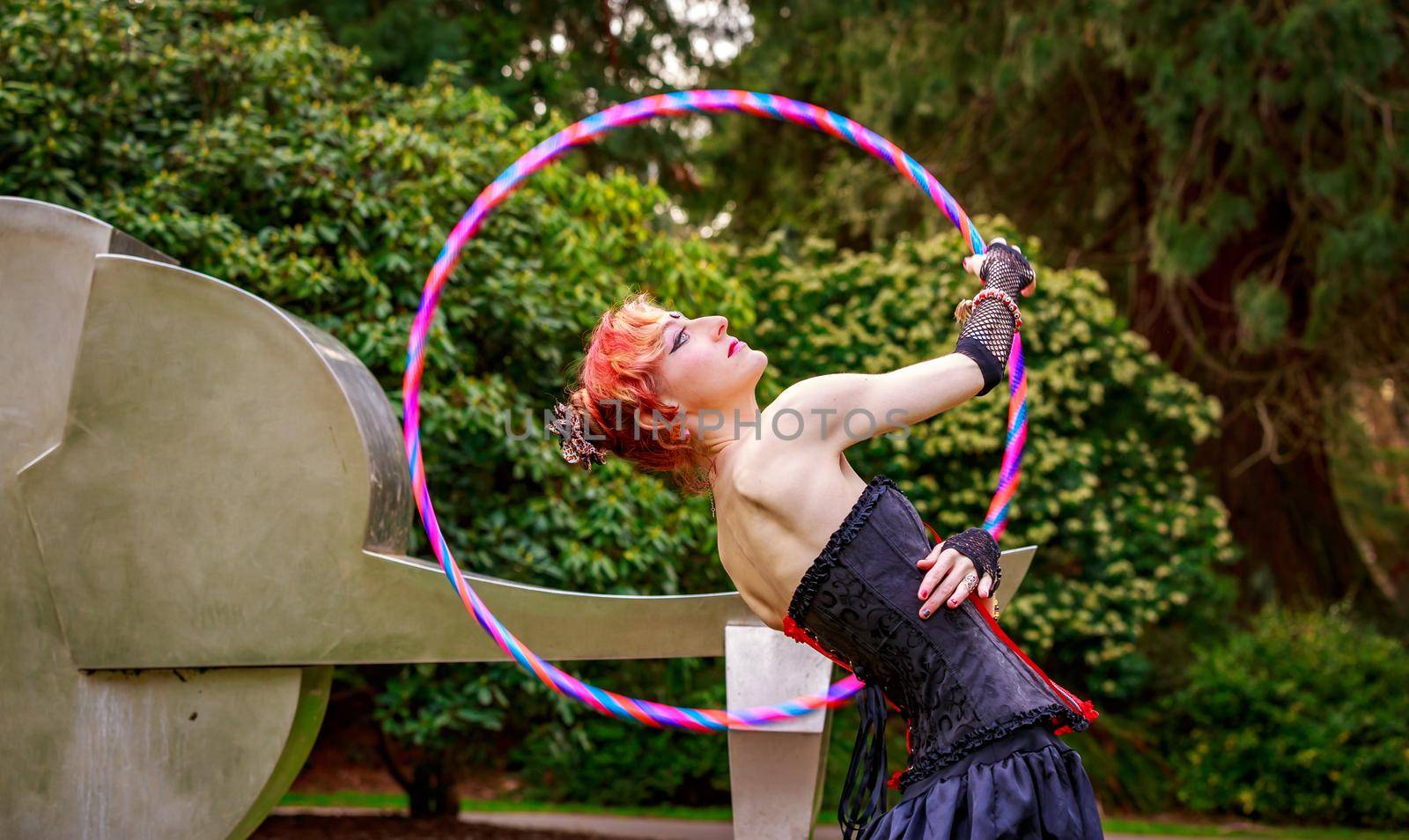 Young beautiful woman in circus costume play with hula hoop in the park.