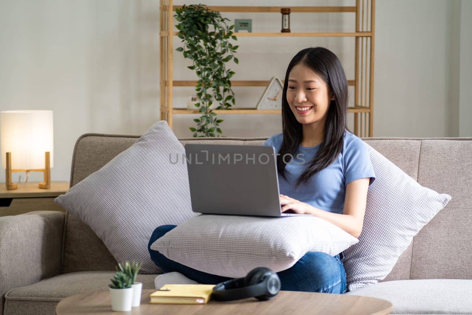 Happy cheerful young asian woman sitting on sofa with laptop, smart beautiful young asian woman chilling in house with laptop. High quality photo