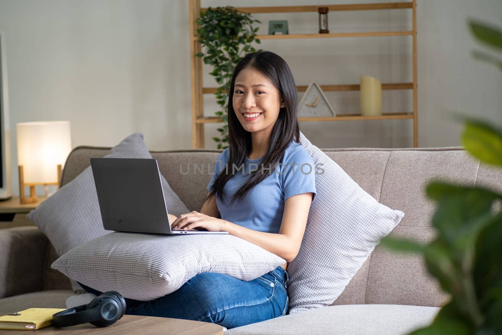 Happy cheerful young asian woman sitting on sofa with laptop, smart beautiful young asian woman chilling in house with laptop. High quality photo