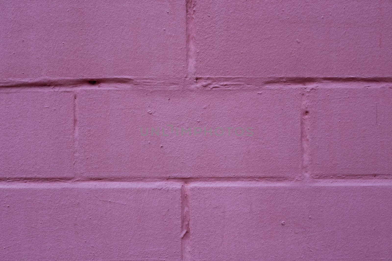 A fragment of a wall made of stone bricks painted in dark pink, red.